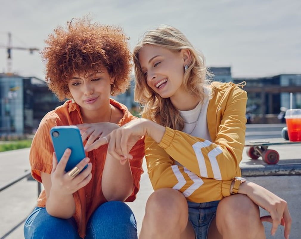 twee vriendinnen kijken naar hun smartphones en glimlachen twee vriendinnen kijken naar hun smartphones en glimlachen